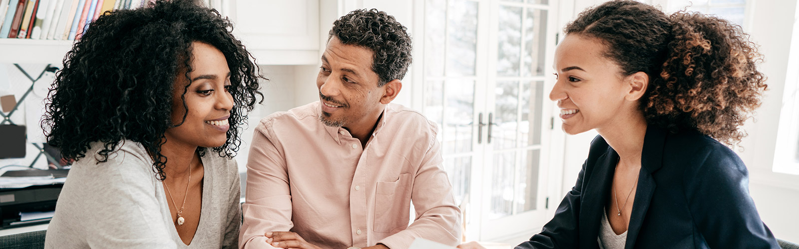 A Black man and Black woman sit smiling across from a Black business woman