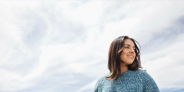 Portrait of young woman standing against sky on sunny day
