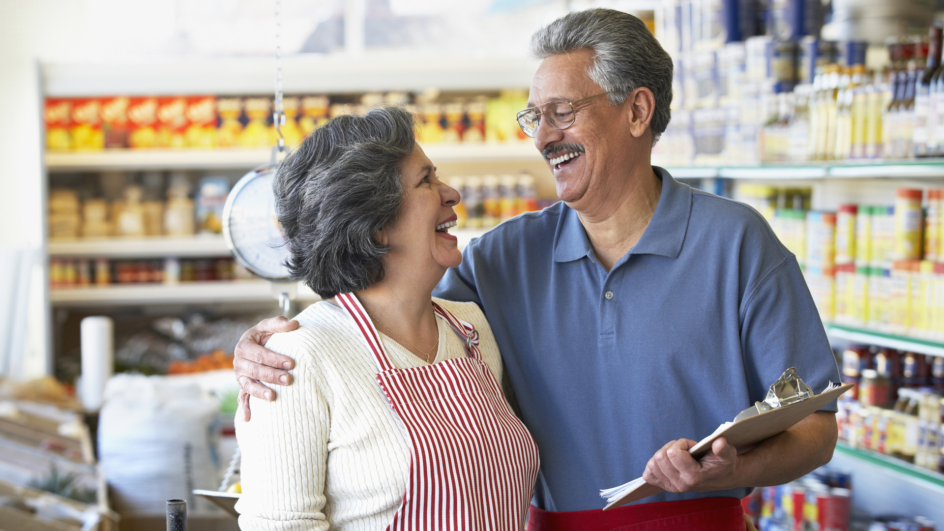 Smiling Hispanic grocery store owners hugging