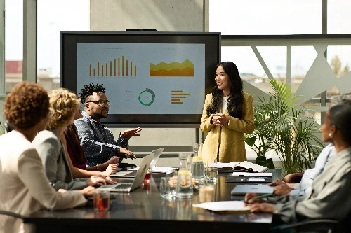 Image of services business professionals having a meeting while a screen in front shows charts and graphs