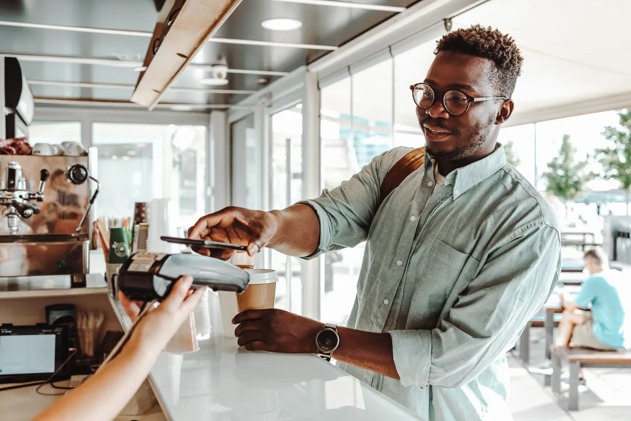Young African American student paying a coffee with his phone 