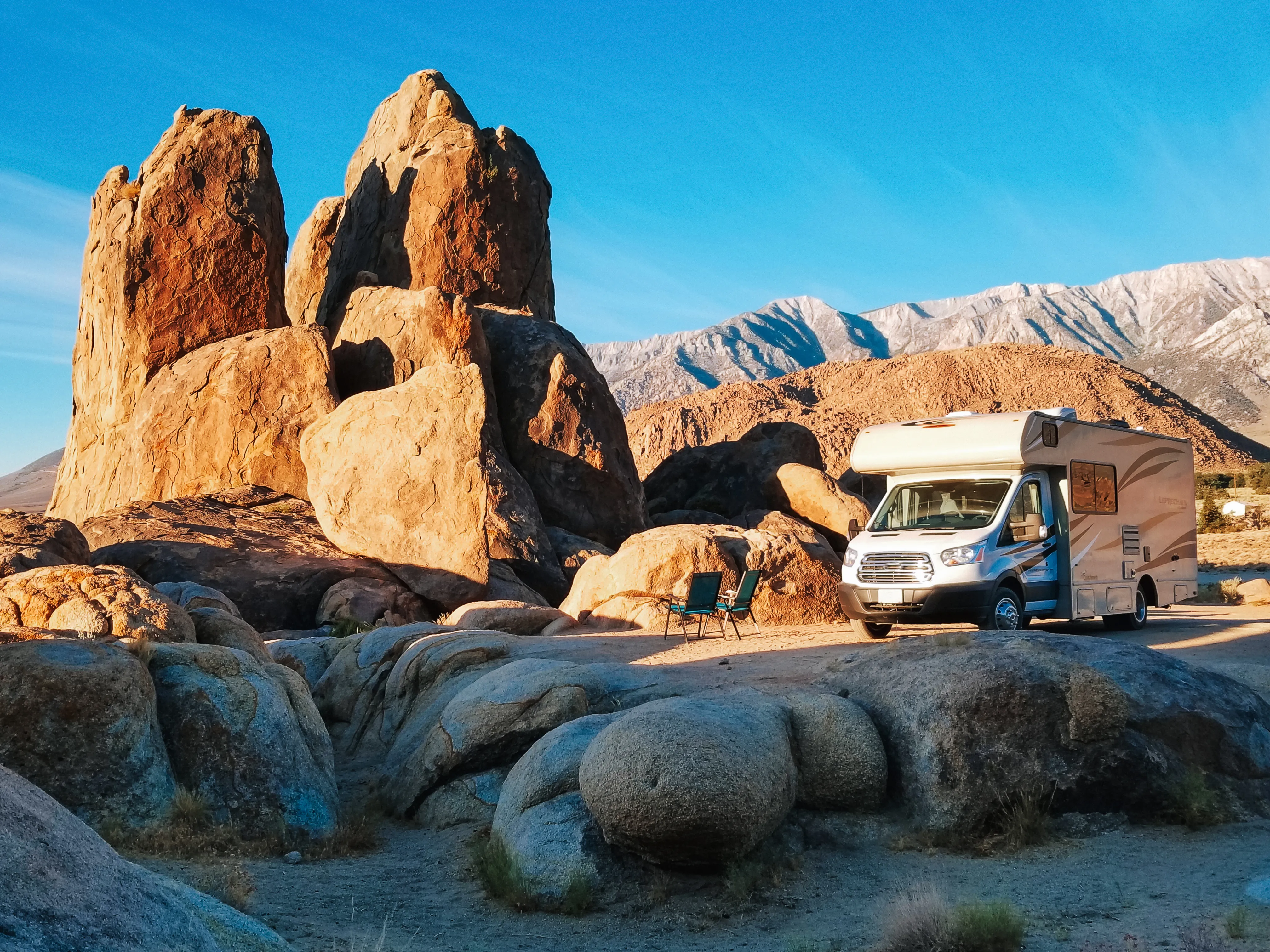 White RV parked in a desert landscape with large rock formations and mountains behind. 