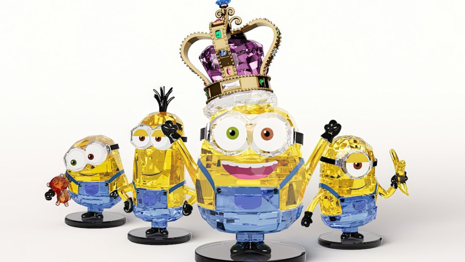 Four Swarovski crystal Minions figurines, including Kevin, Stuart and Bob, displayed on black stands. One Minion wears an ornate crystal crown while the others pose with playful expressions and accessories.