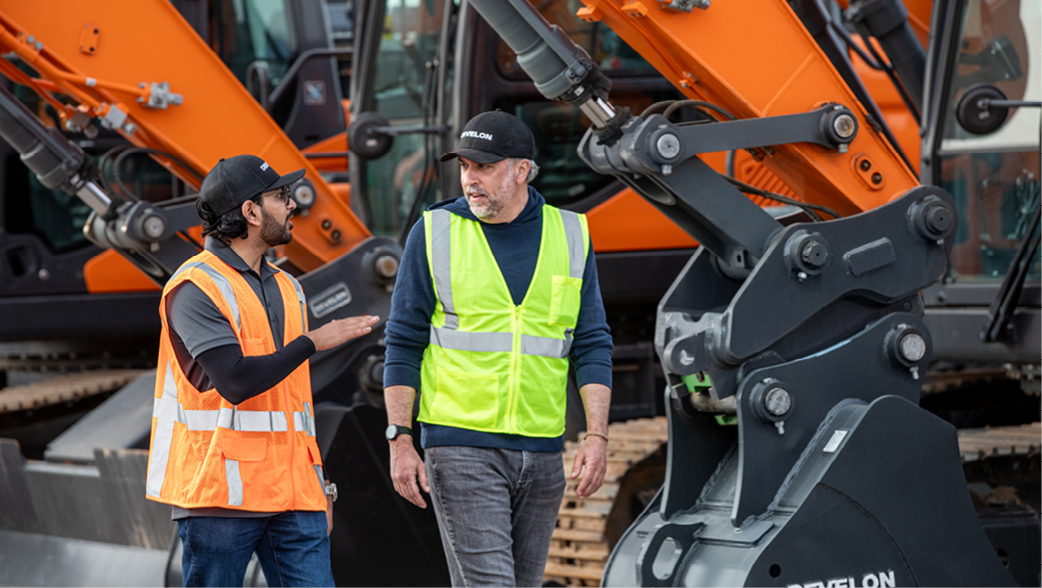 A DEVELON dealer and customer walk and talk near a lineup of DEVELON machines.