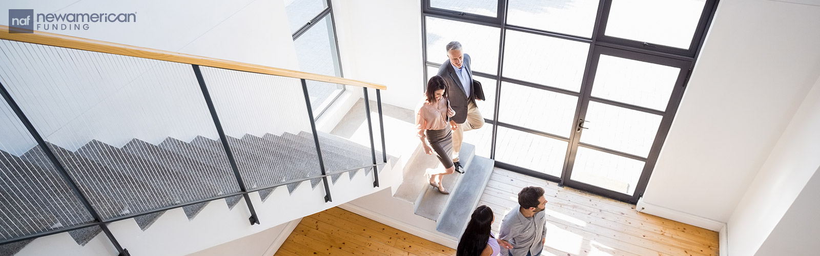 Four adults, dressed in business casual wear, walk down a flight of stairs together talking  