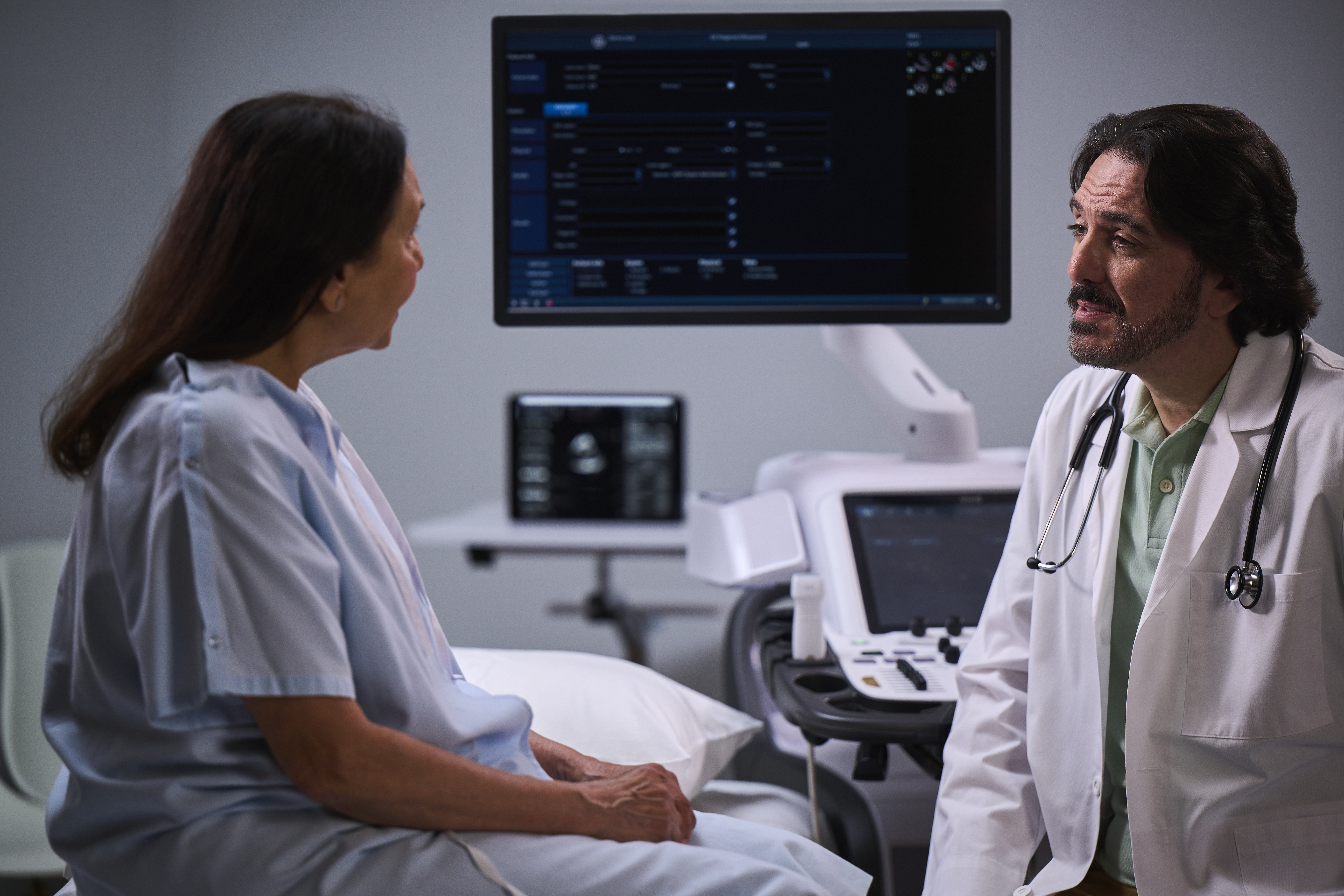 A cardiologist speaks with a female patient while AI in echocardiography works in the background.
