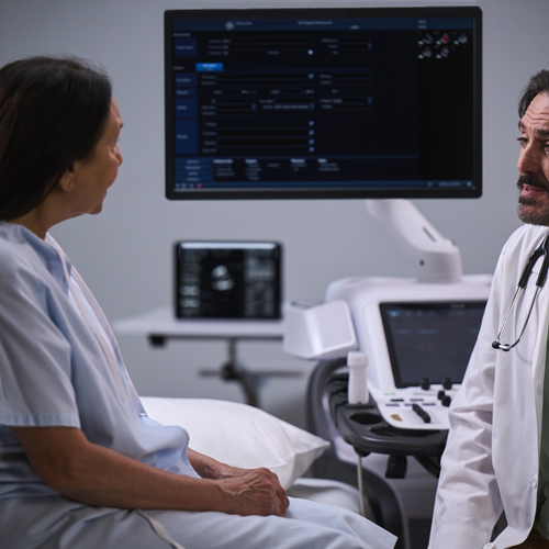 A cardiologist speaks with a female patient while AI in echocardiography works in the background.