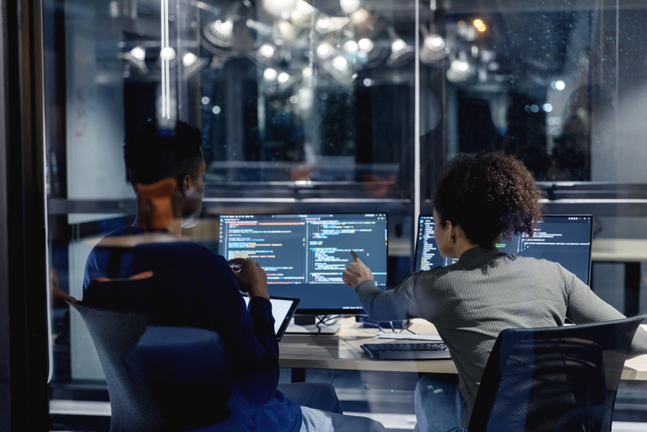 Two colleagues reviewing code on computer screens in an office at night