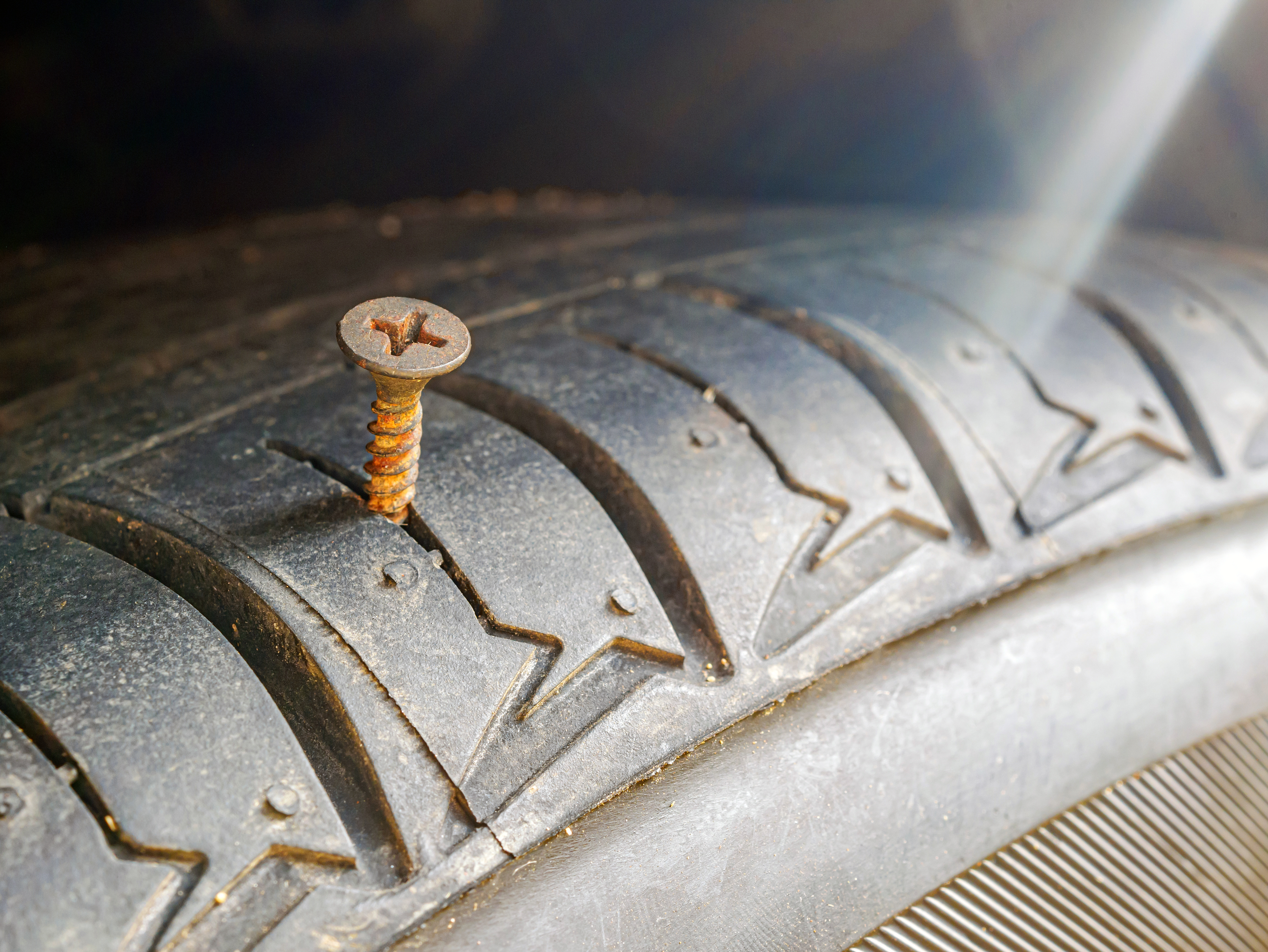 A close-up of a car tyre with a rusty screw embedded in the tread, indicating a puncture.