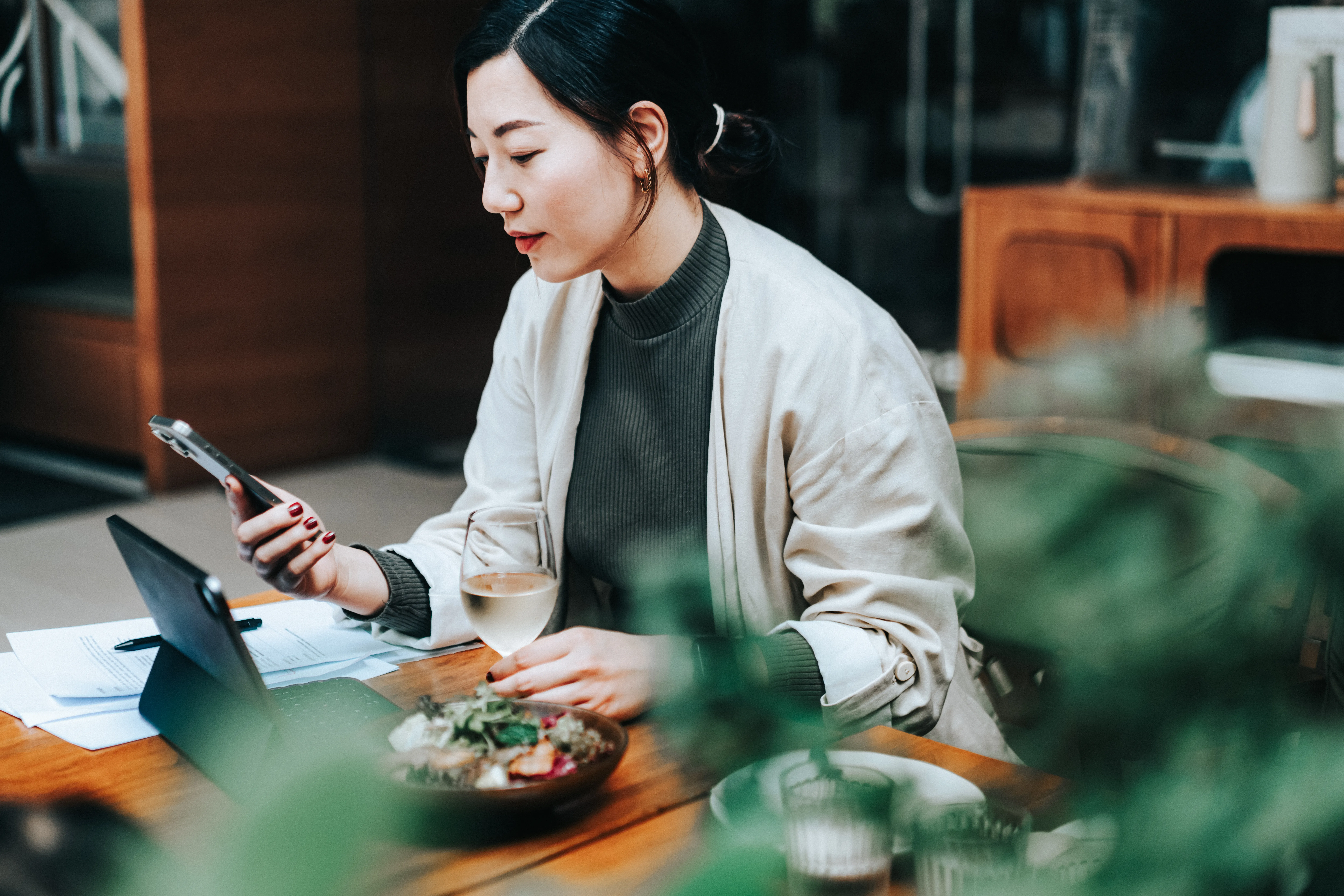 Person sitting at a table using a phone with a meal and drink nearby. 