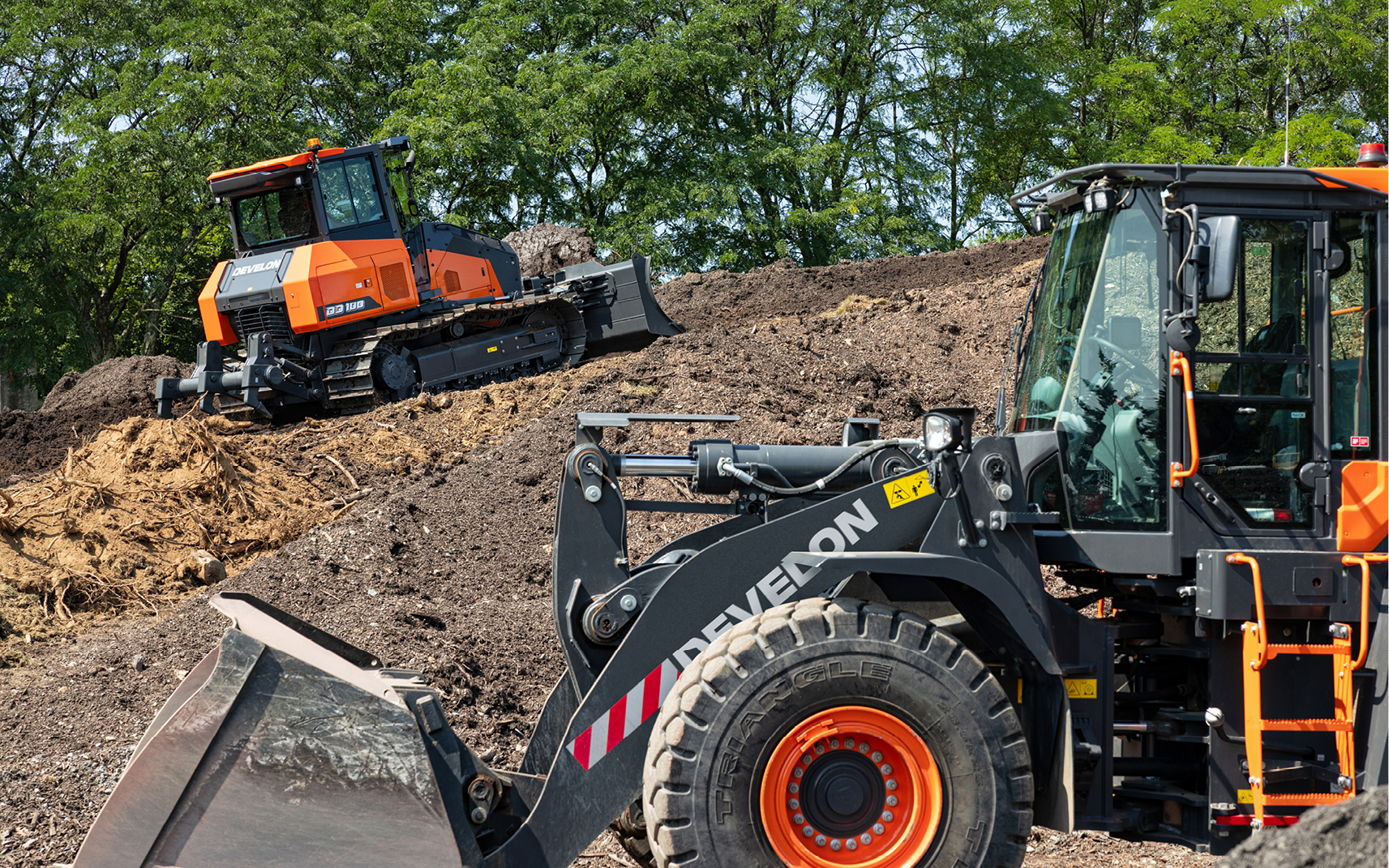 A DEVELON dozer and wheel loader moving dirt on a job site.