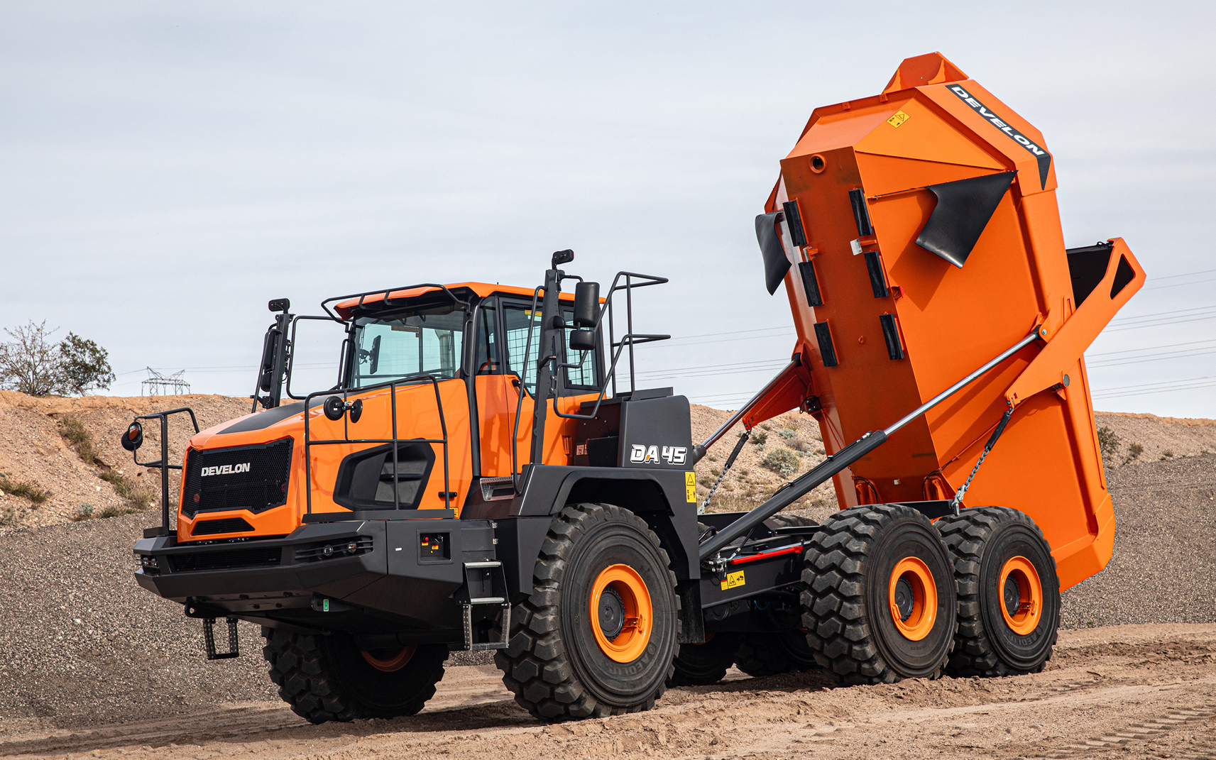 A DEVELON DA45-7 articulated dump truck parked on a dirt construction site with its large dump bed fully raised.