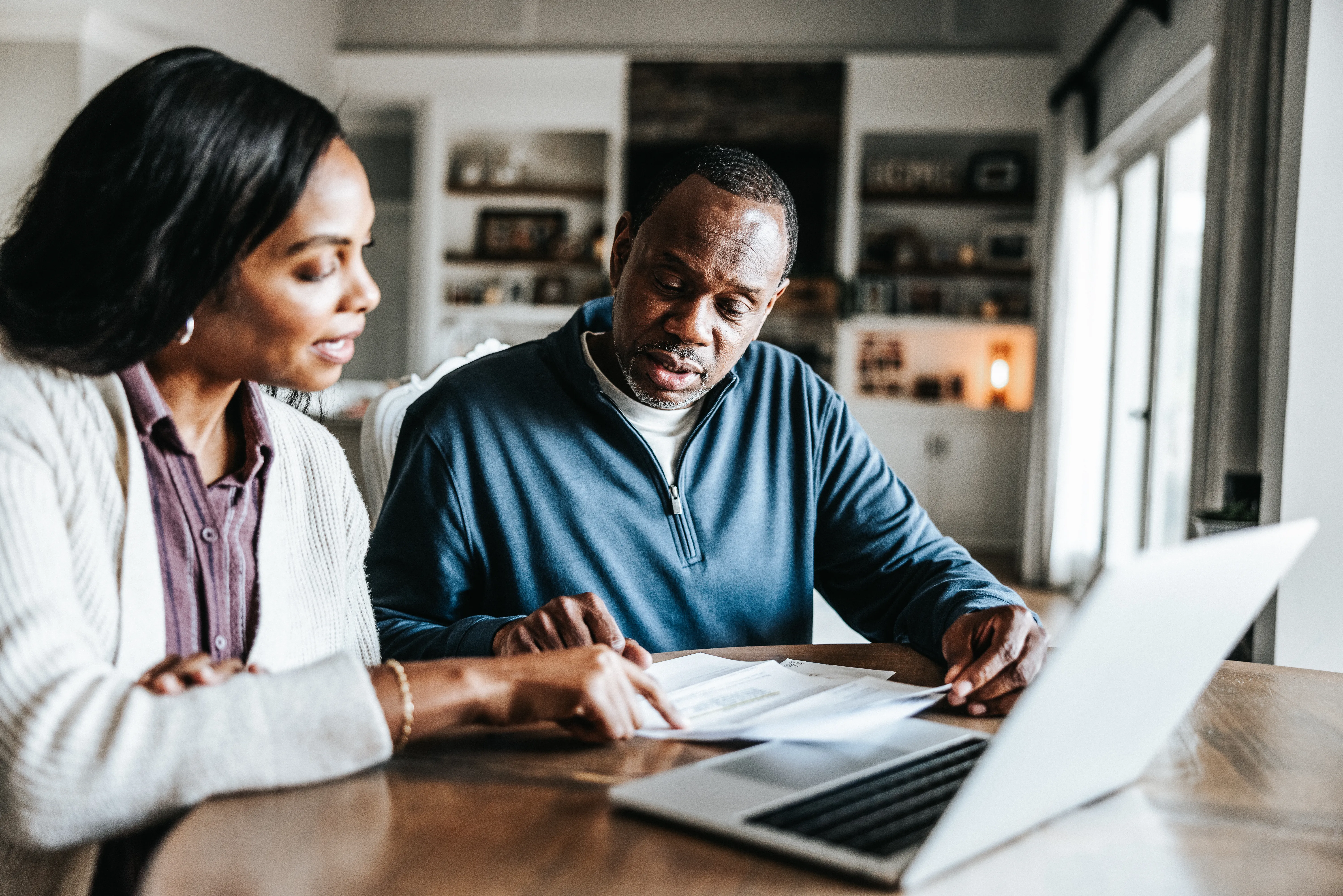Husband and wife looking over bills and using laptop in kitchen. 