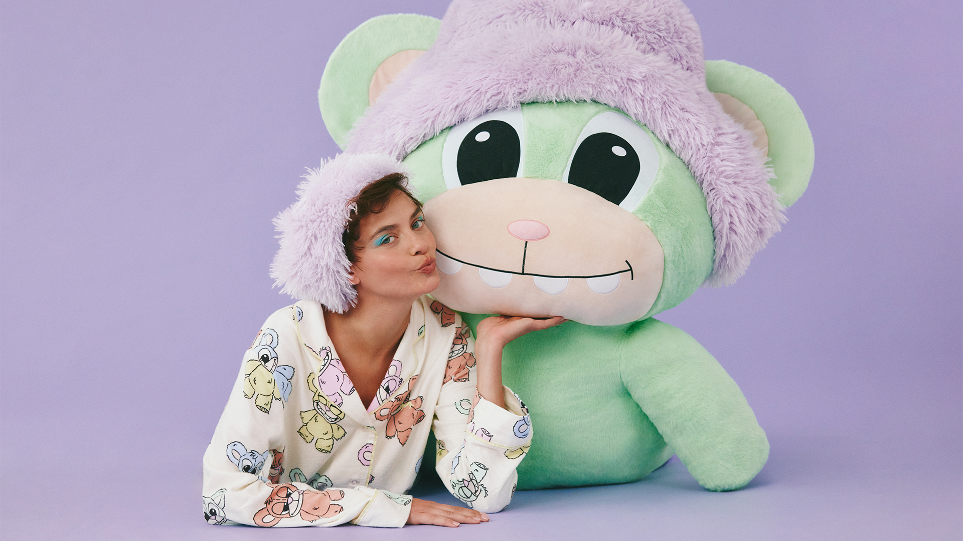 girl in printed pyjamas lying on the ground with a large plush scarebear