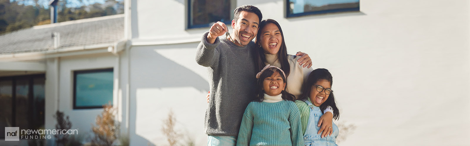 An Asian family stands smiling together holding house keys in front of a home