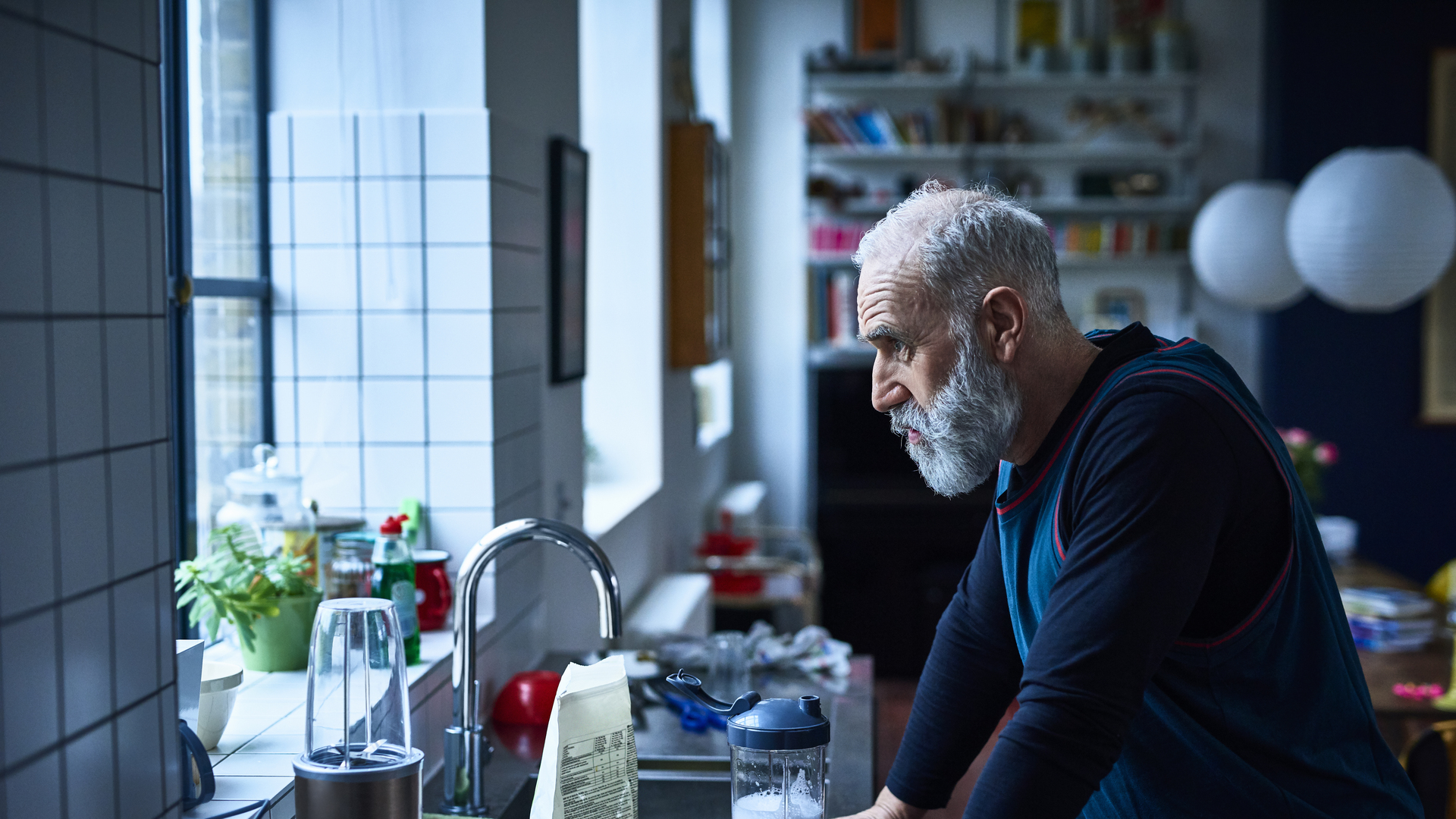 Tired looking senior man leaning on kitchen counter with sports drink