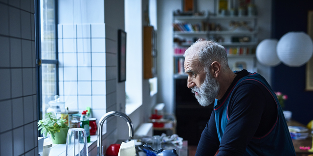 Tired looking senior man leaning on kitchen counter with sports drink