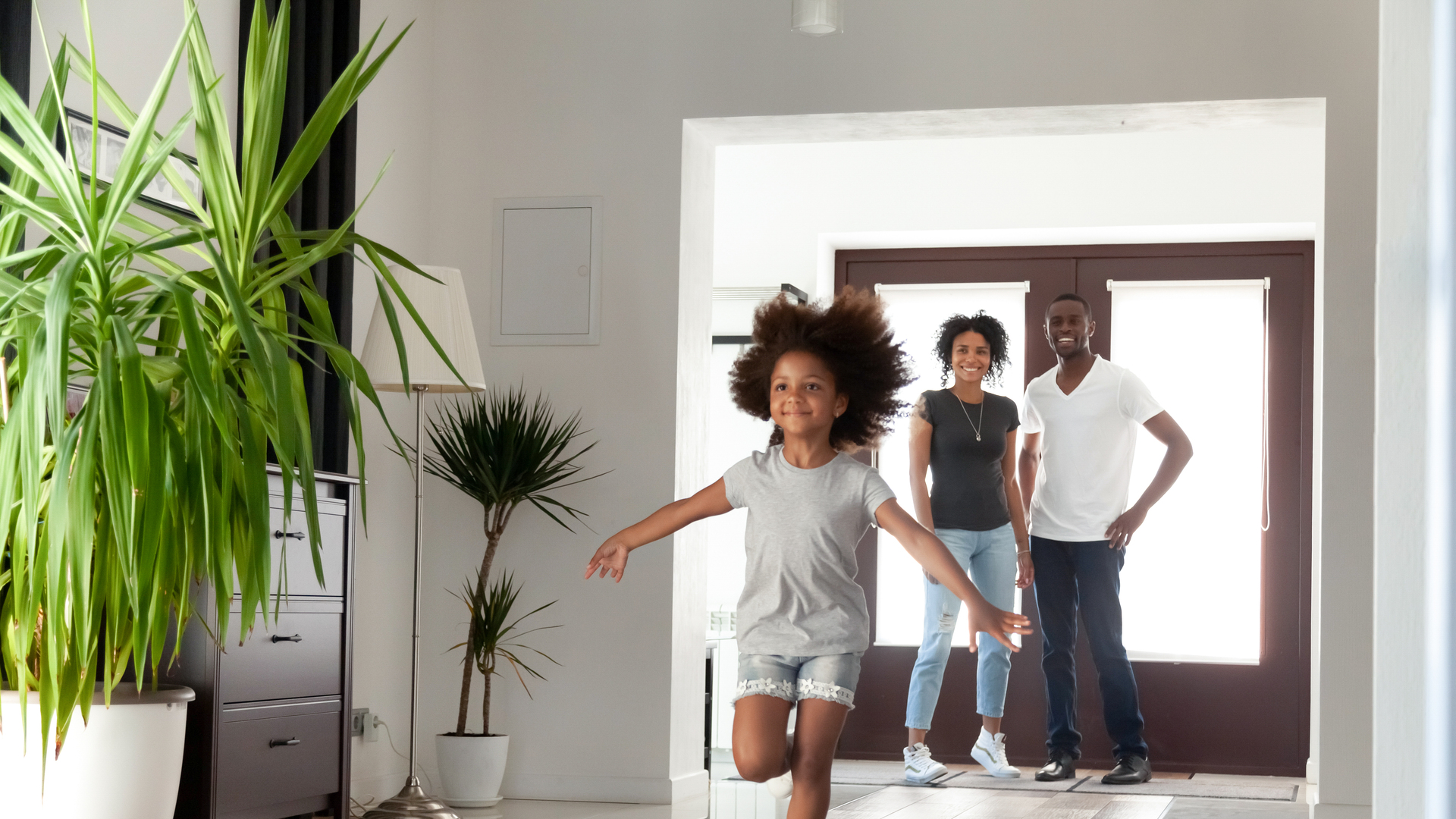 Excited little funny african girl running exploring big modern house on moving day