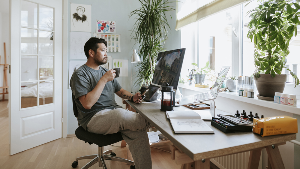 Image of man working from home. Looking at his computer with a coffee.