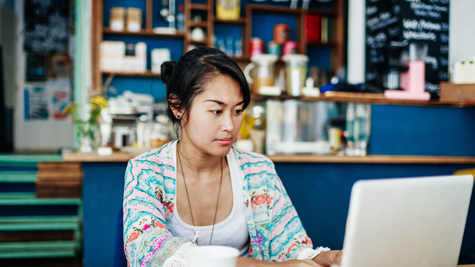 Young Woman Working On Laptop In Colourful Coffee Shop