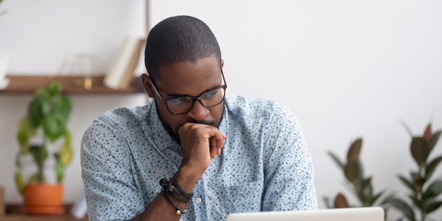 Head shot serious puzzled African American businessman looking at laptop