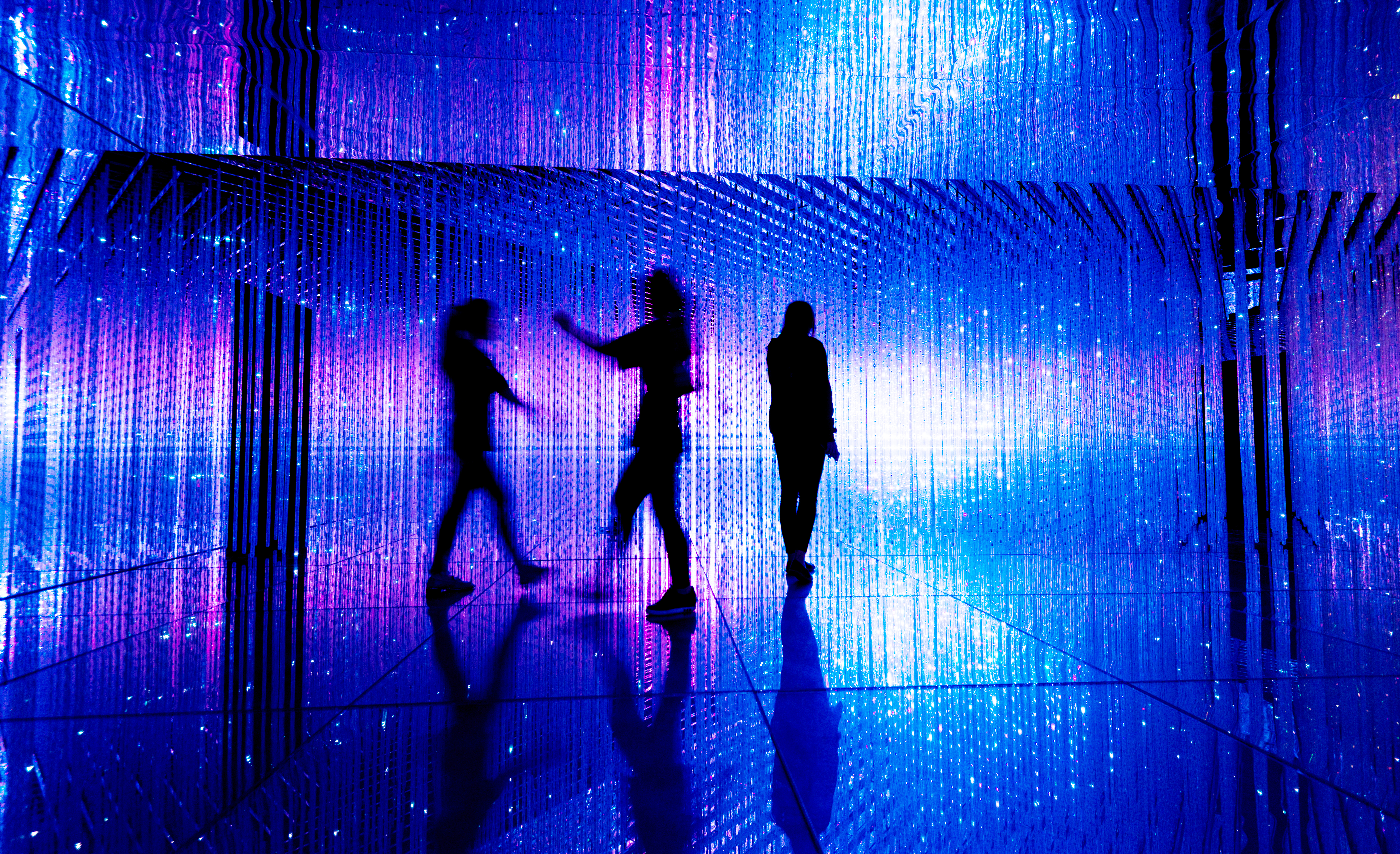 Three people walk through an immersive experience of blue and purple light using AV technology and 4k projectors to facilitate visual learning.