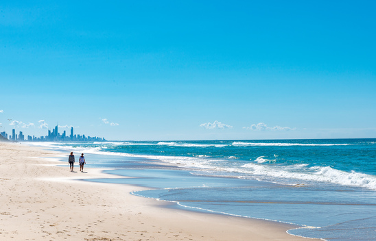 Two people walking on Mermaid Beach with the Gold Coast cityscape in the background