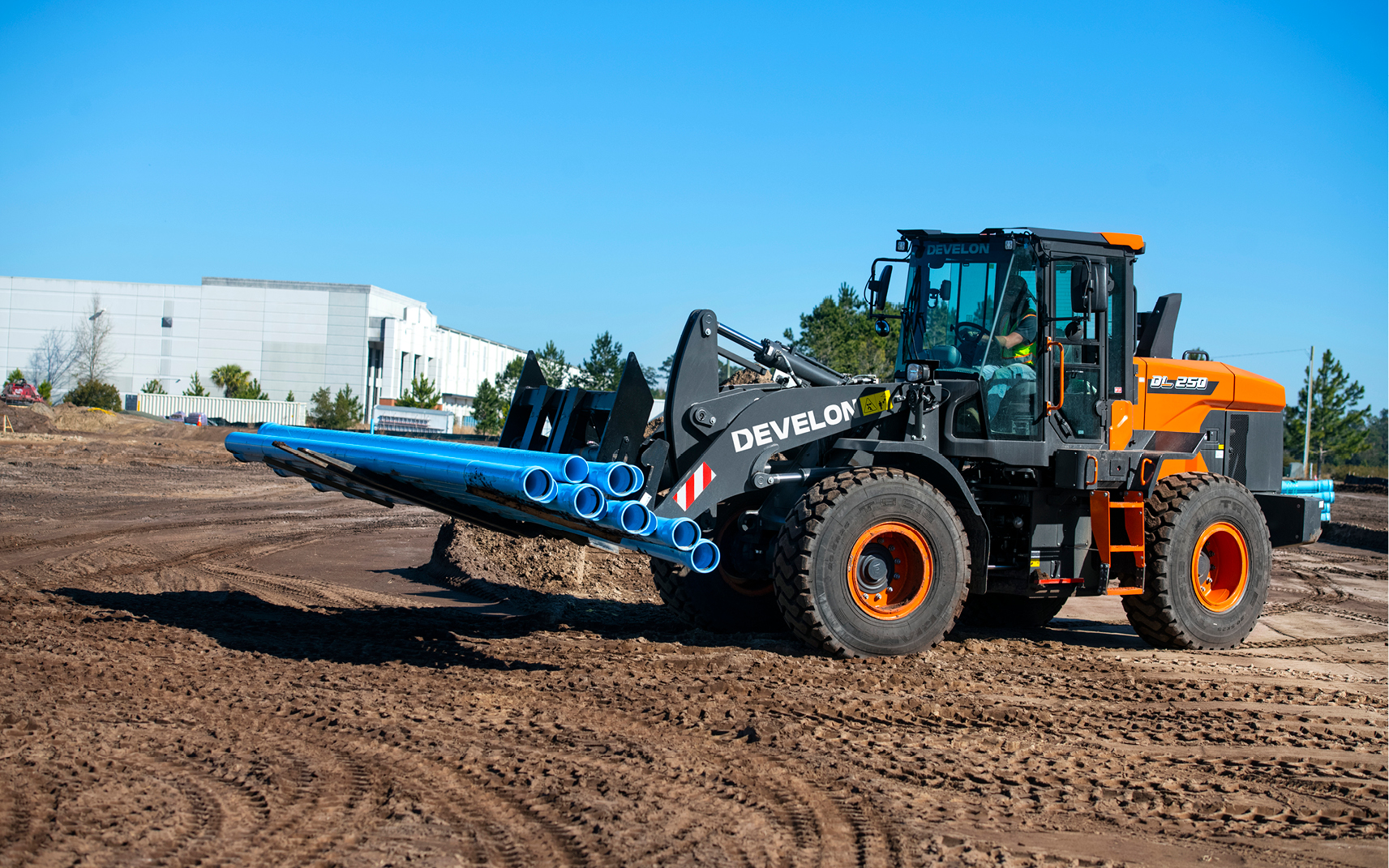 A DEVELON wheel loader is paired with a pallet fork to carry pipes for new underground construction.