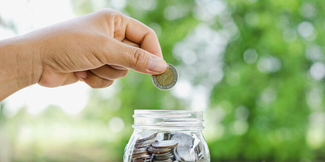 female hand putting money coins in jar concept and green nature background