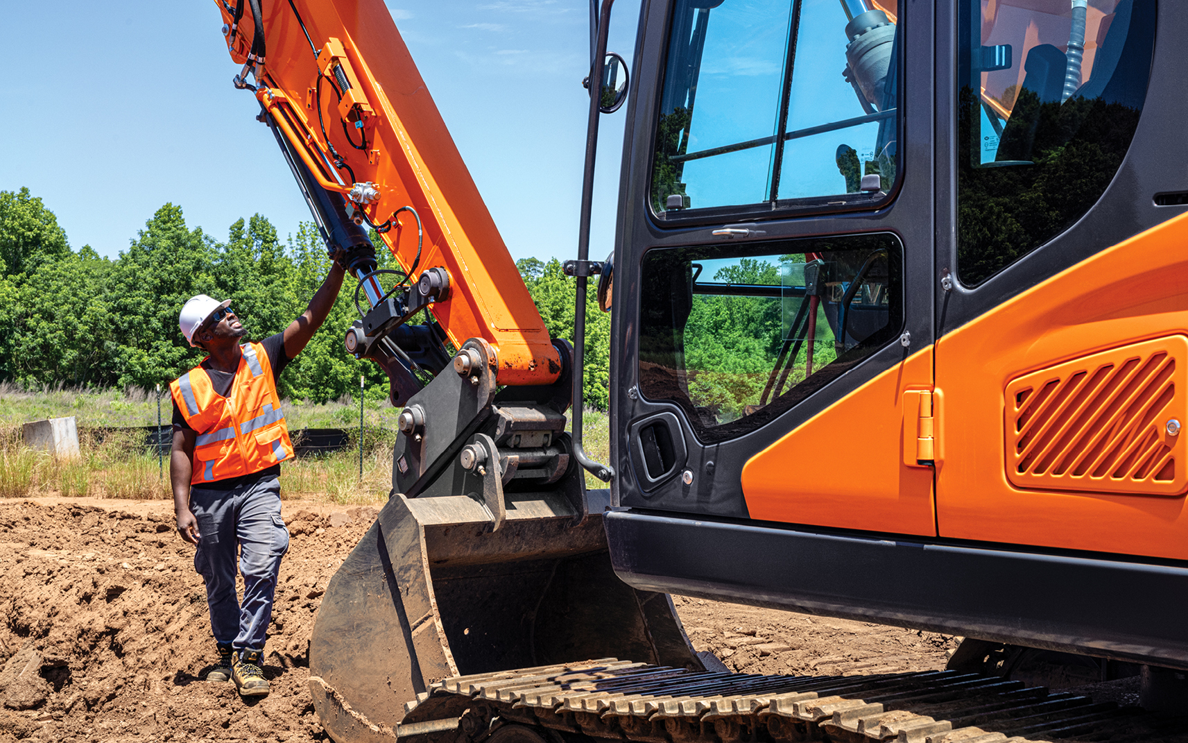 An operator walks around a DEVELON crawler excavator and reviews a hydraulic maintenance checklist.