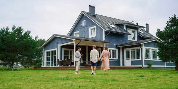 A woman in a suit and a man and a woman wearing casual clothes and holding hands talk in front of a blue house