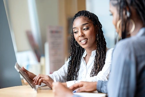Image of two services industry professionals looking at a screen on a tablet and chatting