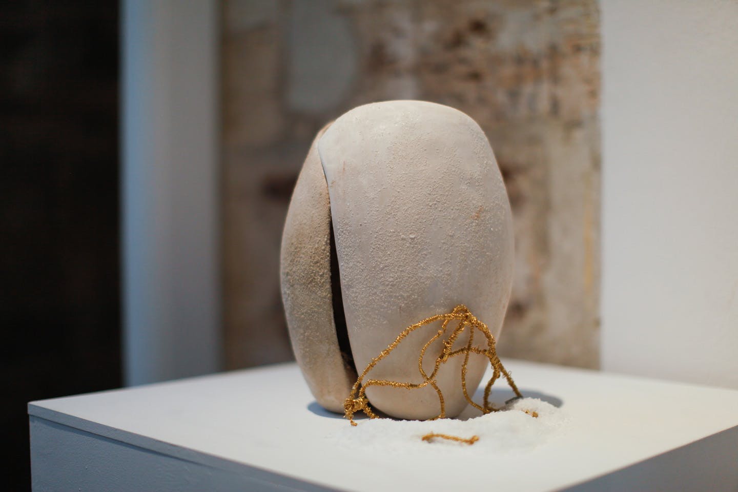 Abstract stone-like sculpture with golden string detail on pedestal