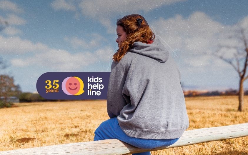 A girl sits on a fence in the country and stares off into the distance.
