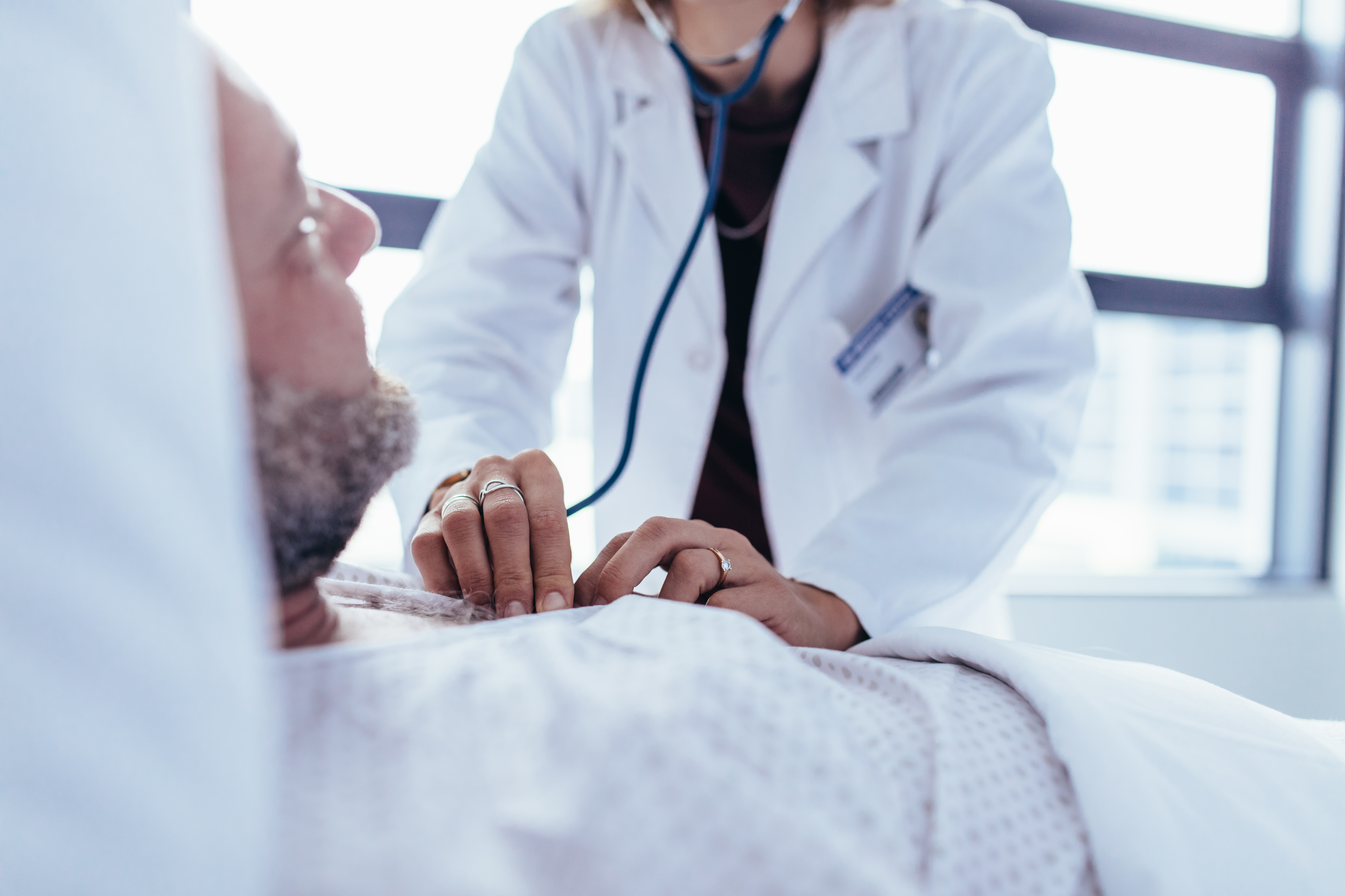 Close up female doctor hand checking heart rate of male patient. Doctor checking the pulse of a patient lying on a hospital bed.