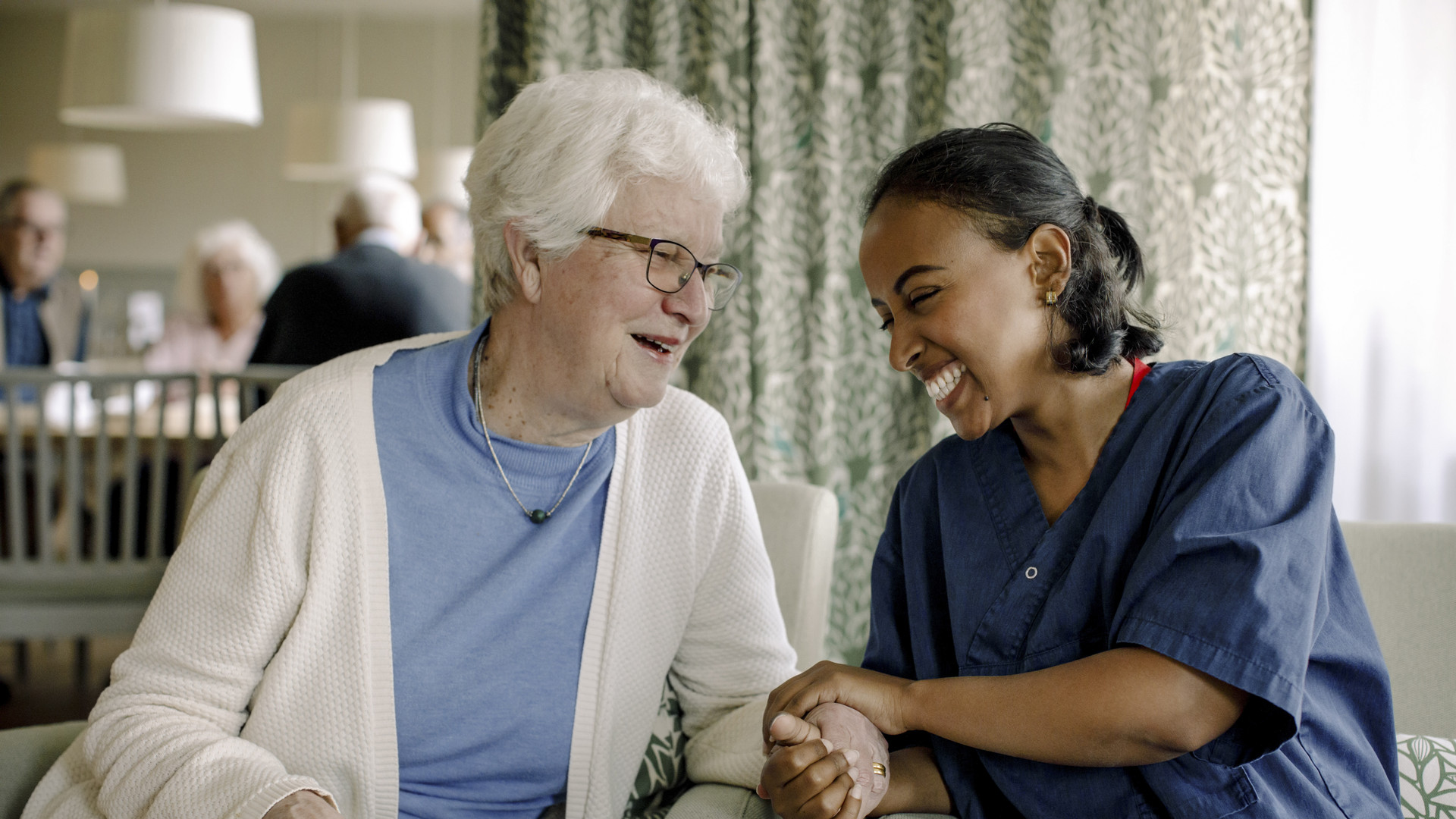Cheerful female nurse holding hand of senior woman sitting at retirement home