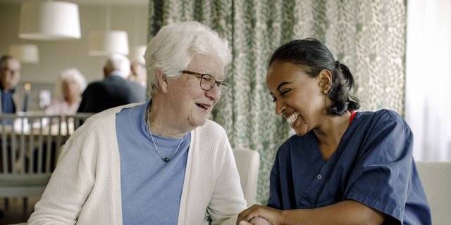 Cheerful female nurse holding hand of senior woman sitting at retirement home