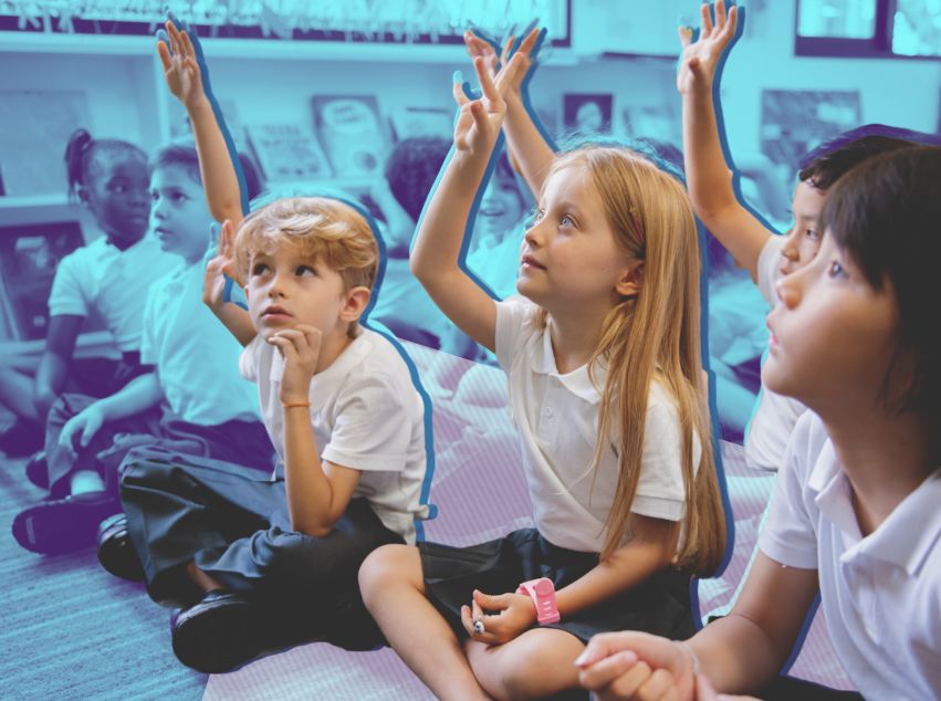 Young school kids put their hand up while sitting in their classroom