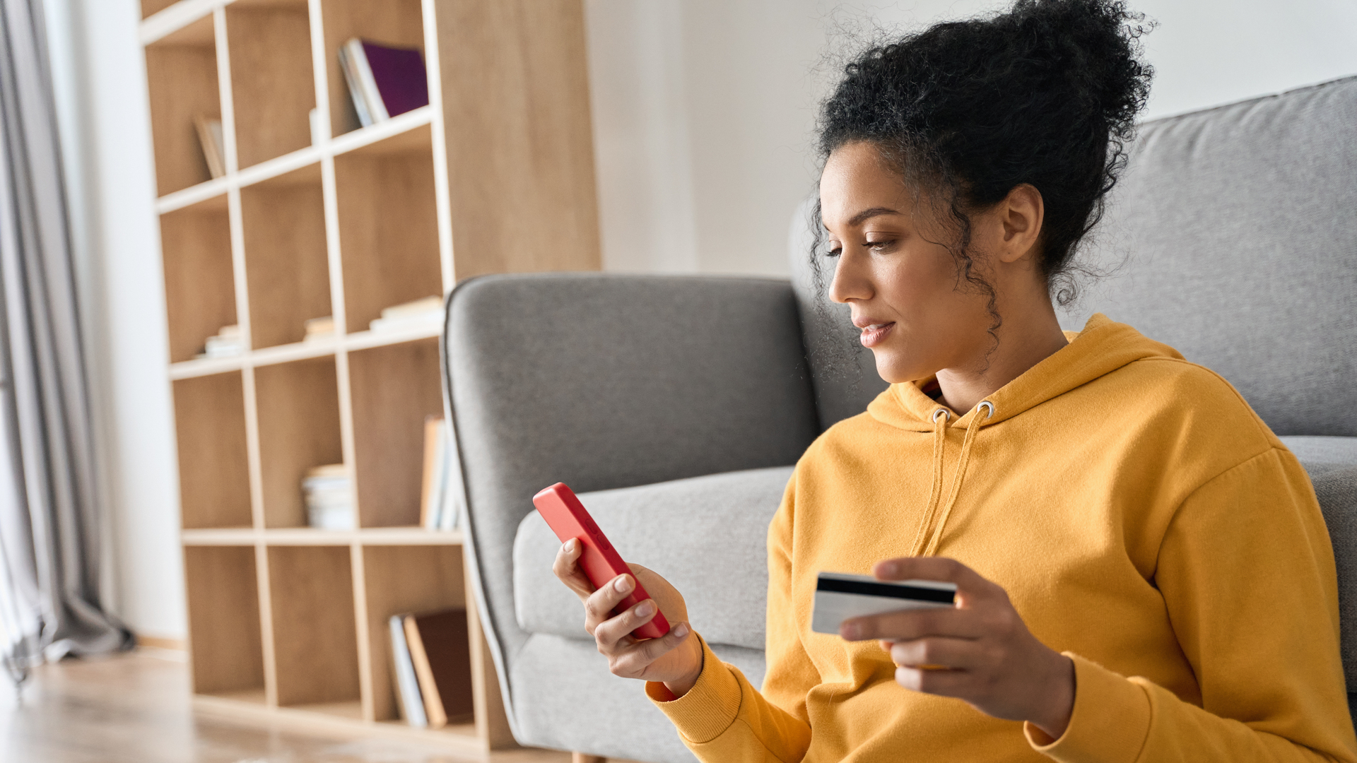 Young adult African american girl sitting indoors doing mobile payment online.