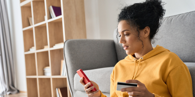 Young adult African american girl sitting indoors doing mobile payment online.