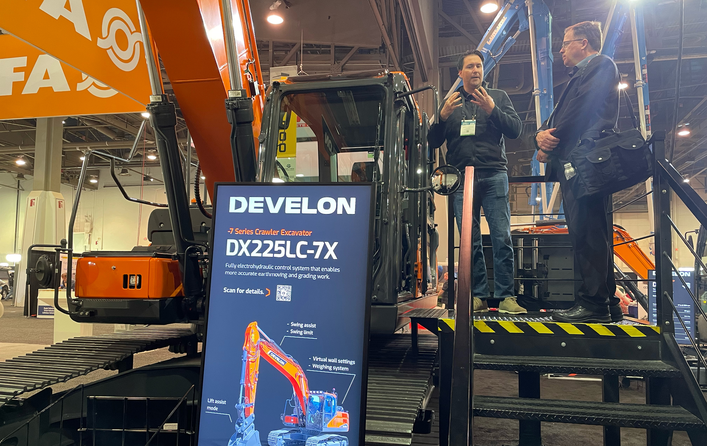 DEVELON representative speaks with attendee about DX225LC-7X crawler excavator.