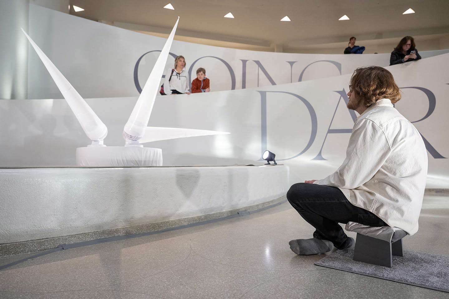 A visitor shown seated in the Guggenheim Museum observes an inflatable sculpture students installed in the museum’s lobby.