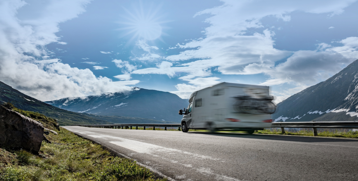 An RV driving along a road with mountains in the background