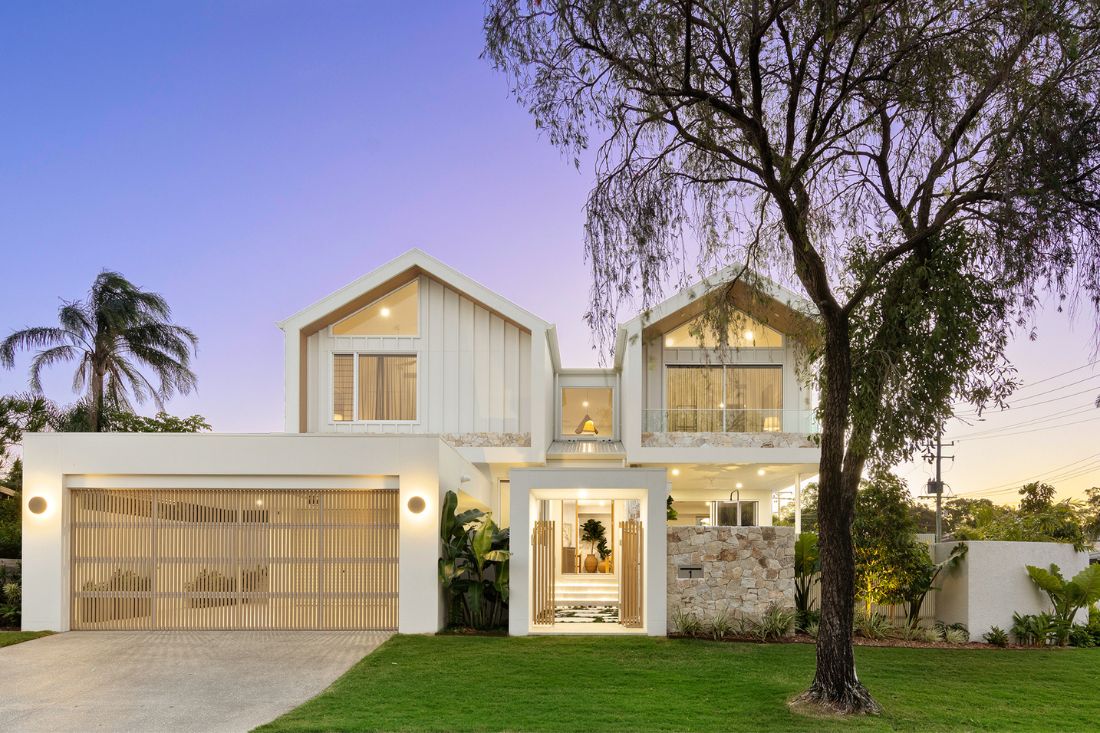 External front of a 2 level white home with driveway and gardens at dusk.
