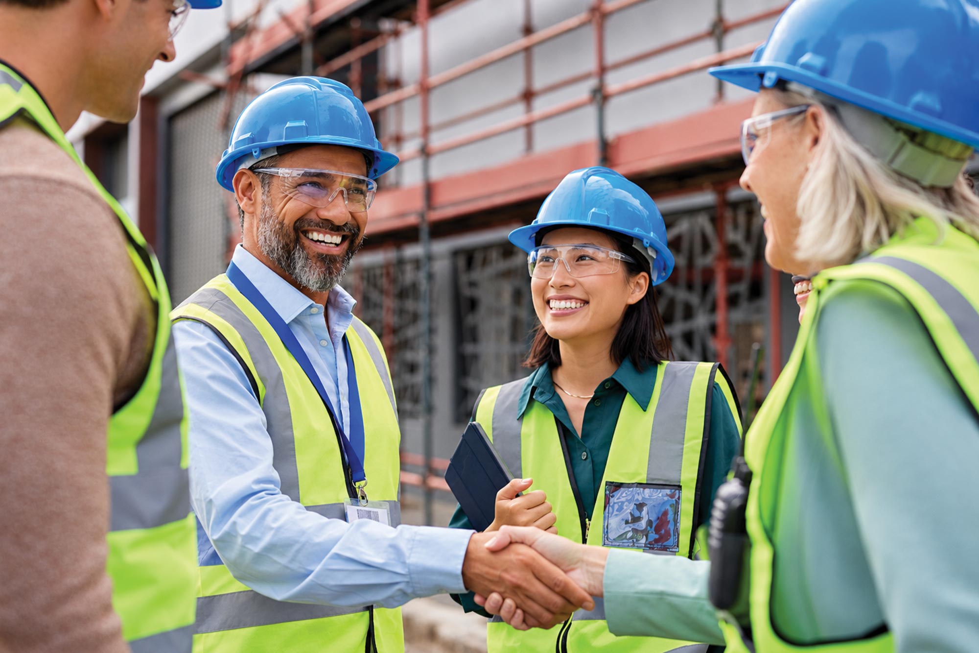 Group of ICT professionals in hard hats and safety vests shaking hands at an outdoor project site