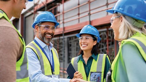 Group of ICT professionals in hard hats and safety vests shaking hands at an outdoor project site