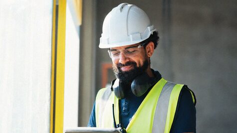 Smiling telecommunications technician wearing personal protective equipment reviewing site plans on a digital tablet