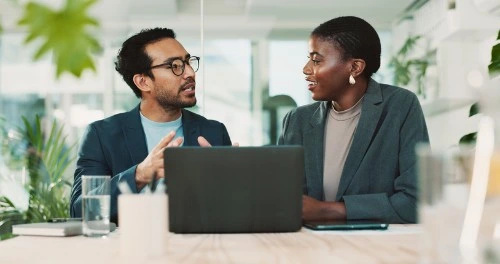 Business leaders having a focused conversation at a desk with a laptop in a modern office setting
