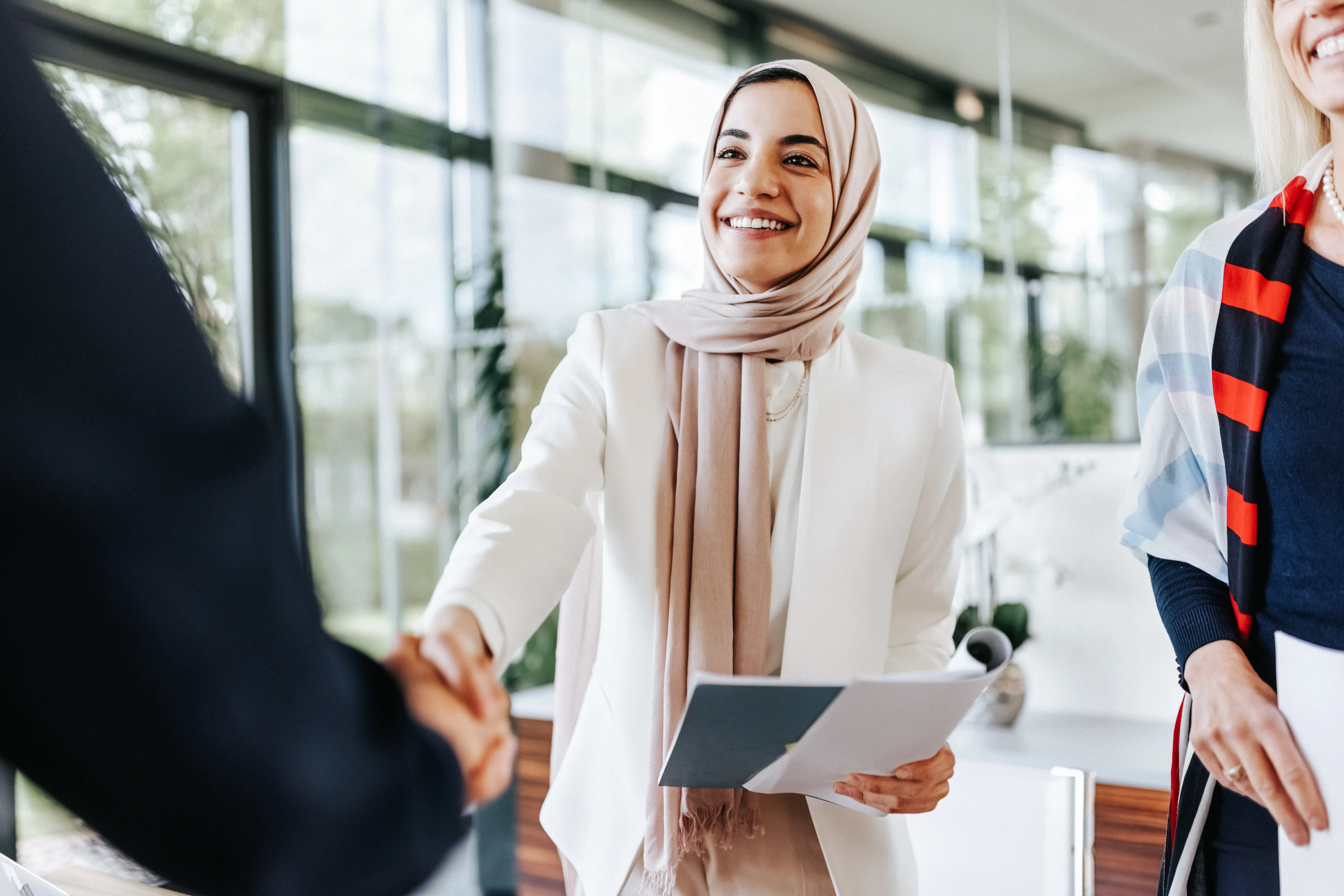 Middle Eastern business woman shaking the hand of business professional in brightly lit office 