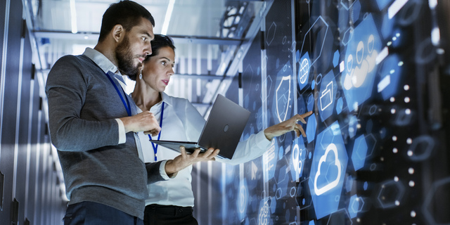 Male IT Specialist Holds Laptop and Discusses Work with Female Server Technician. They're Standing in Data Center, Rack Server Cabinet with Cloud Server Icon and Visualization.